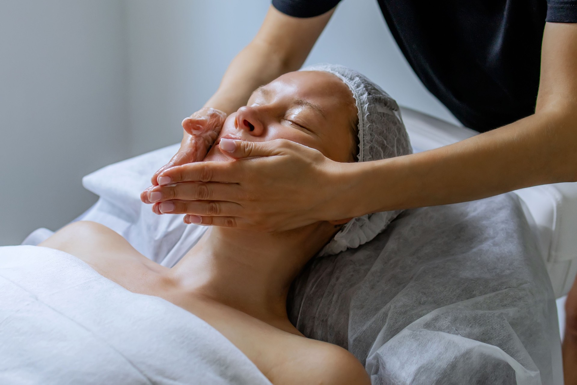 Middle aged female receiving facial massage in beauty salon. Anti aged massage and skincare concept with a beautiful woman. Hands of cosmetology specialist making facial lifting massage in SPA salon